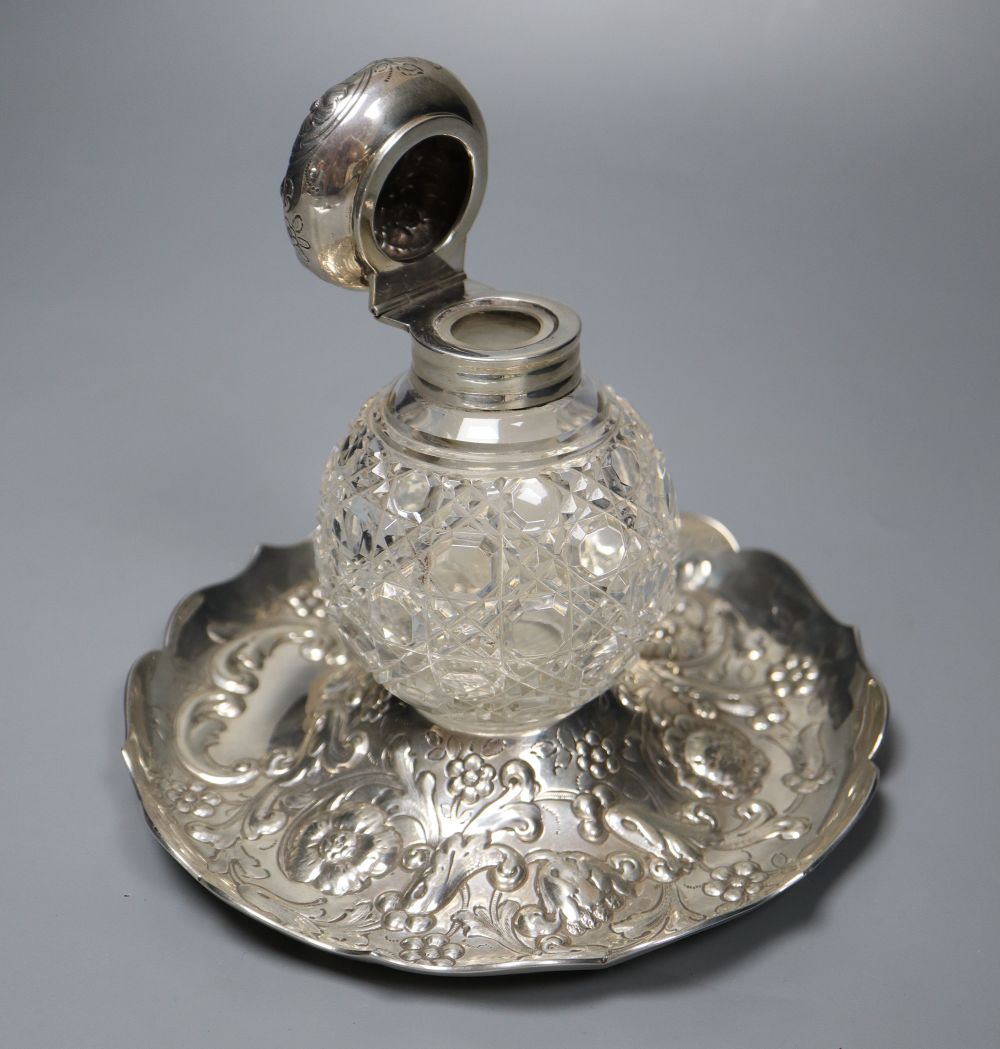 A late Victorian repousse silver mounted glass inkwell, on a repousse silver stand, London, 1891, height 14.4cm.